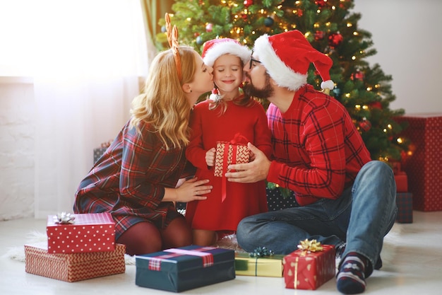 幸せな家族の両親と子供の娘がクリスマスの朝にプレゼントを開く