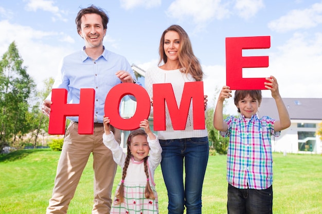 Счастливая семья родителей и детей перед своим домом на открытом воздухе с буквами HOME