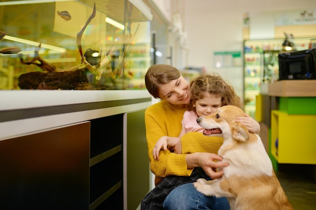 Photo happy family at pet shop with their loving corgi dog. mother and daughter shopping at vet store choosing new pet like fish