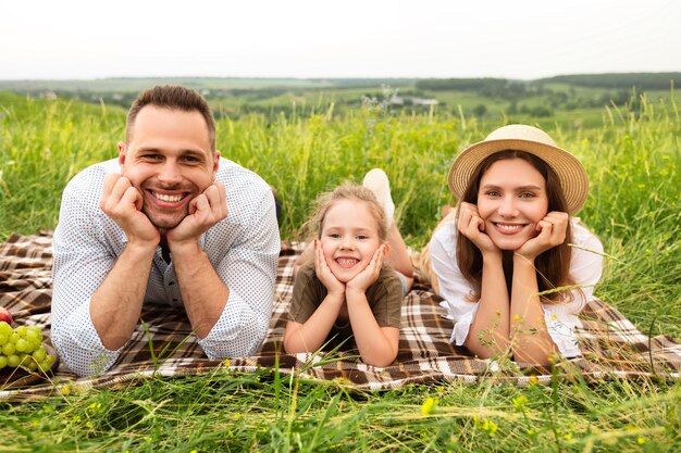 ピクニックで幸せな家族。笑顔の両親と田舎で一緒に時間を過ごすカメラでポーズをとるかわいい赤ちゃん