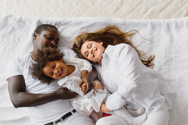 幸福的家庭和他们的女儿玩在床上照片