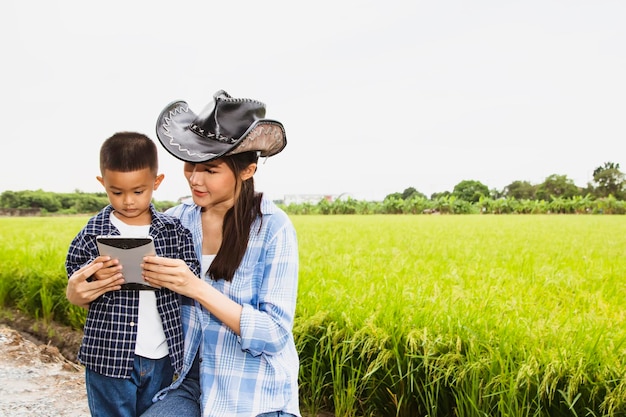 Фото Счастливый семейный портрет, мать-фермер и сын учат мальчика милому сыну с помощью планшета на рисовом поле.
