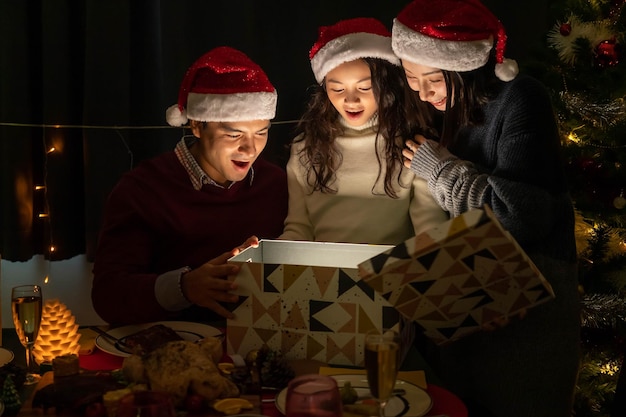 Felice ritratto di famiglia padre madre e figlia festeggiano insieme natale e capodanno aprendo la confezione regalo con magica sorpresa