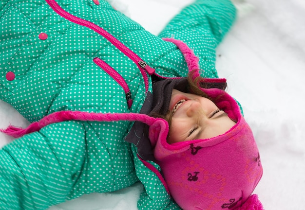 Happy family - portrait little girl lying on the snow and laughing at the winter day