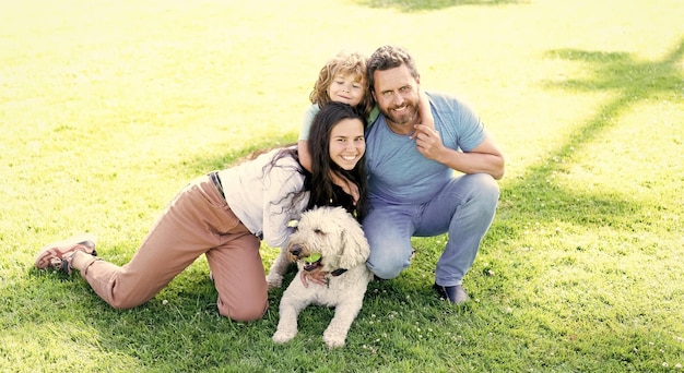 Happy family portrait of mom dad and kid boy playing with pet in park on green grass togetherness