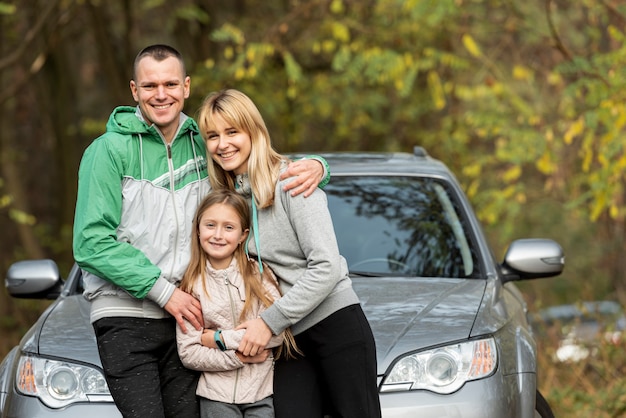 Happy family posing in front of car