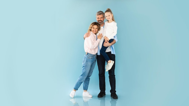 Happy family posing hugging father holding little daughter blue background