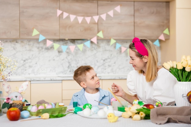 Foto famiglia felice che si prepara per la pasqua bambino carino con la madre che dipinge le uova attività domestica concetto di unità e amore mamma e figlio