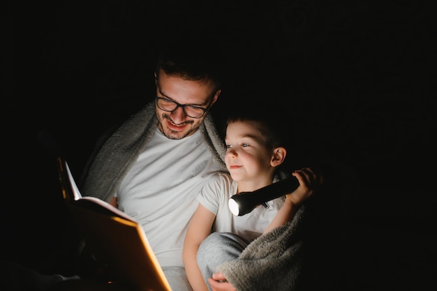 Happy family reading bedtime story under blanket in evening Father and son spend time together Father's Day