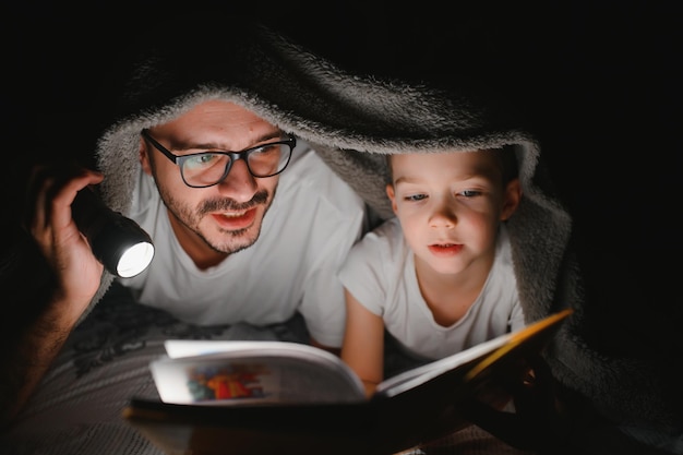 Photo happy family reading bedtime story under blanket in evening father and son spend time together father's day