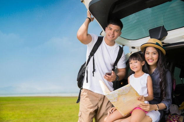 Happy family reading map while sitting in car trunk on field against sky