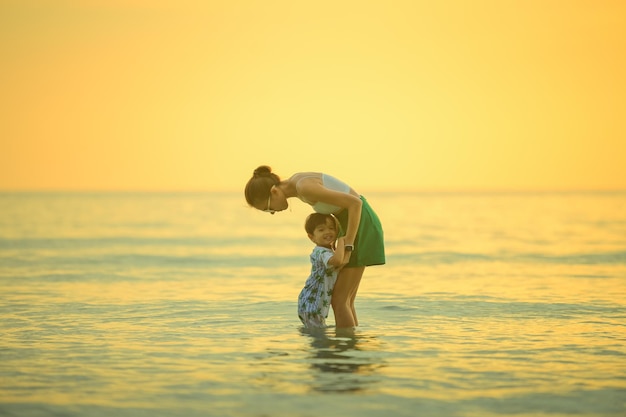 Foto famiglia felice che riposa in spiaggia in estate madre e bambino piedi al mare schiuma alla luce del sole l'acqua si sta muovendo