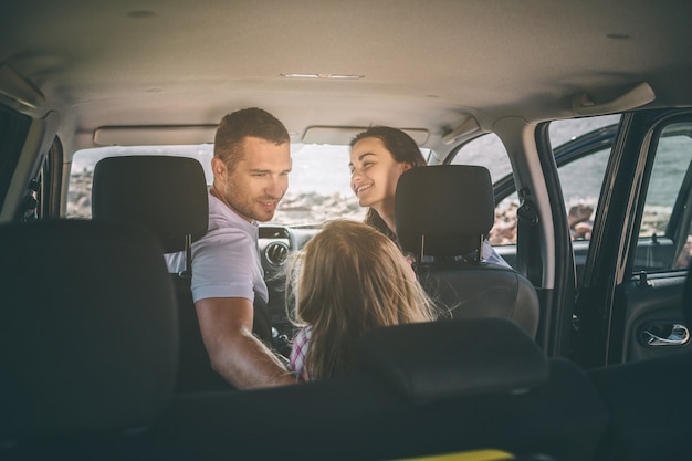 Happy family on a road trip in their car. Dad, mom and daughter are traveling by the sea or the ocean or the river. Summer ride by automobile