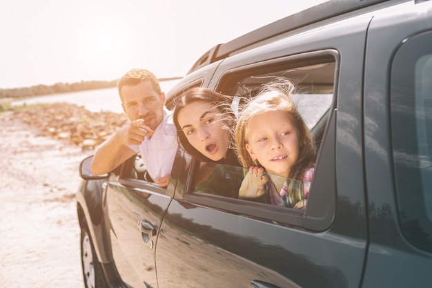 Happy family on a road trip in their car. Dad, mom and daughter are traveling by the sea or the ocean or the river. Summer ride by automobile