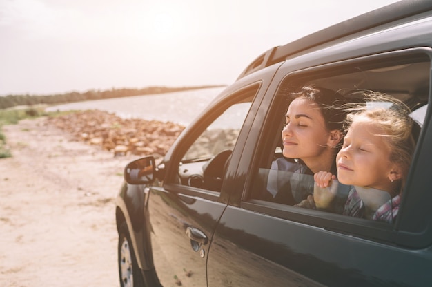 車での遠征で幸せな家族。お父さん、お母さん、娘は海や海、川で旅行しています。自動車による夏の乗り物