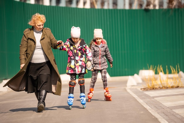 A happy family in roller skates, grandma teaches two granddaughters to roller-skate