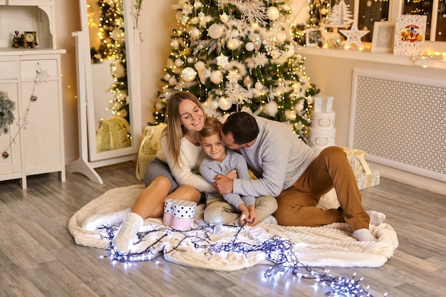 クリスマスツリーのそばに座っている幸せな家族。