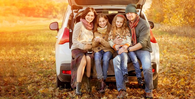 Happy family sitting in car trunk on autumn forest