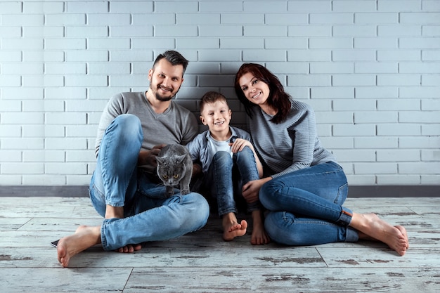 Happy family sitting on the floor against the gray wall.