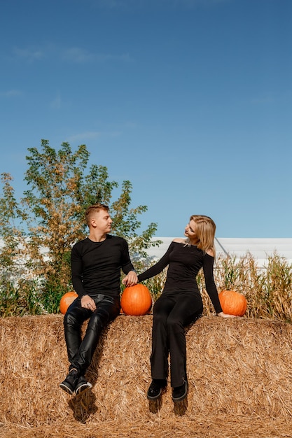 Happy family sitting on hay bales and holding pumpkins at outdoor market. Autumn time.