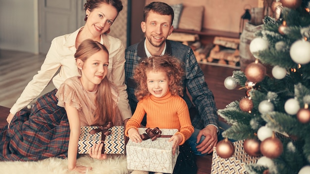 아늑한 거실에 있는 크리스마스 트리 근처에 앉아 있는 행복한 가족. 휴일 개념