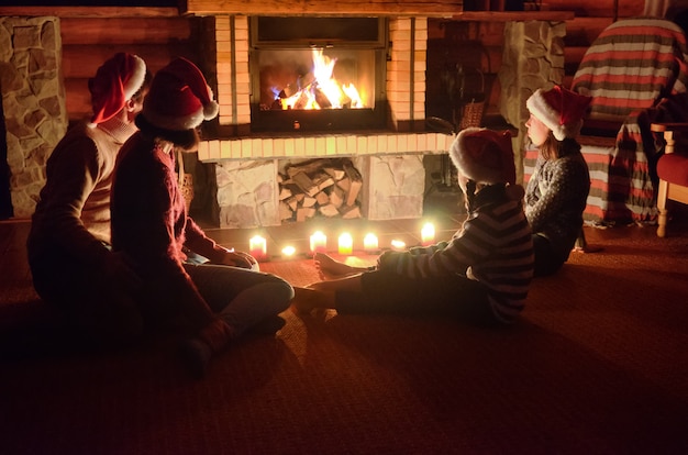 Photo happy family sitting near fireplace at home and celebrating christmas and new year, parents and children in santa hats