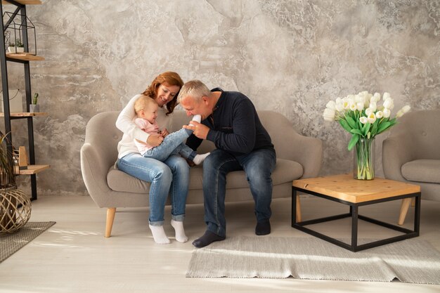 Happy family sitting on the sofa with baby girl. Grandfather and grandmother spend their day together with granddaughter indoor