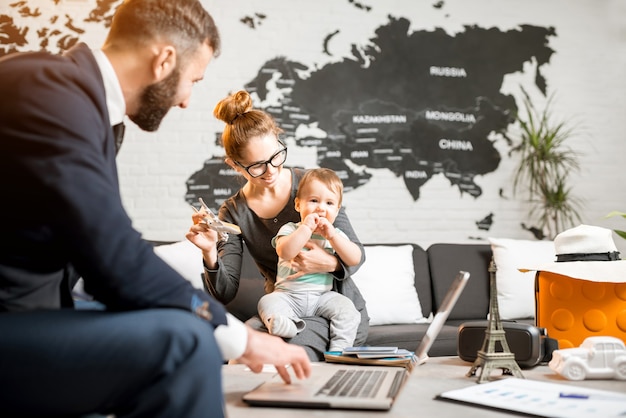 Happy family sitting with man agent at the travel agency office with beautiful map on the background choosing a tour for a summer vacation