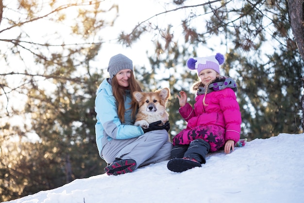 Happy family - smiling mother and daughter with little cute corgi fluffy puppy at the winter day