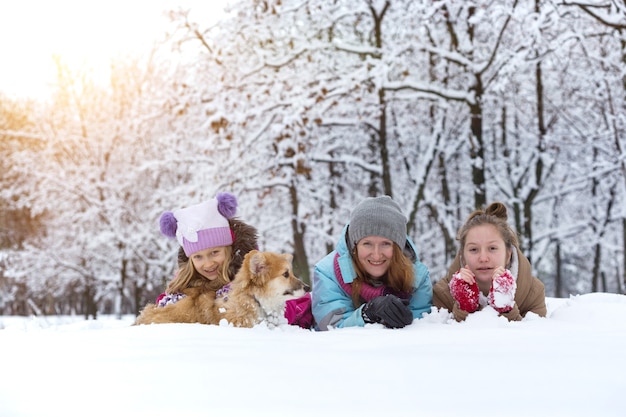 Famiglia felice - madre e figlie sorridenti con un piccolo e grazioso cucciolo di corgi al giorno d'inverno