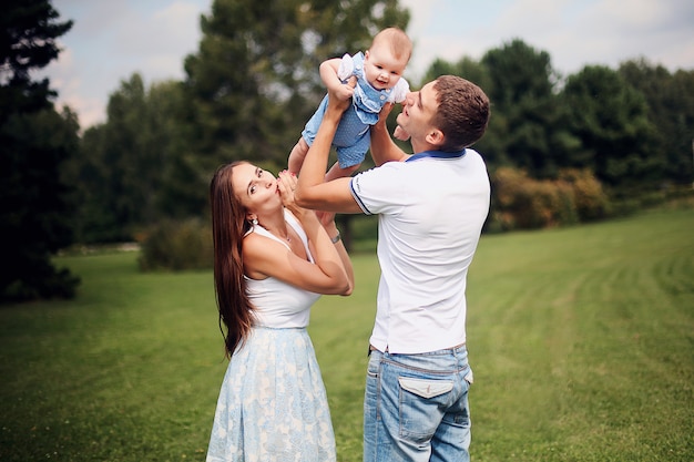 Happy family. Smiling parents kissing their child. Handsome father and beautiful mother hold their little  daughter in their arms in the park. Young man and woman.