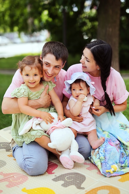 Happy family. Smiling parents with children. Handsome man and beautiful woman with little daughters having fun in summer park. 