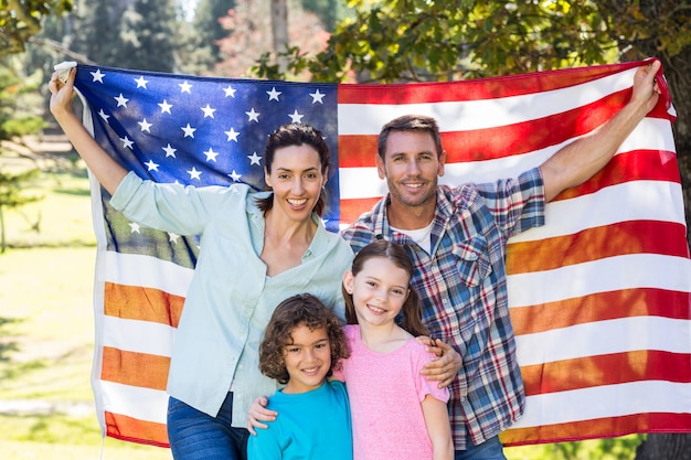 写真 公園でアメリカの旗で笑っている幸せな家族