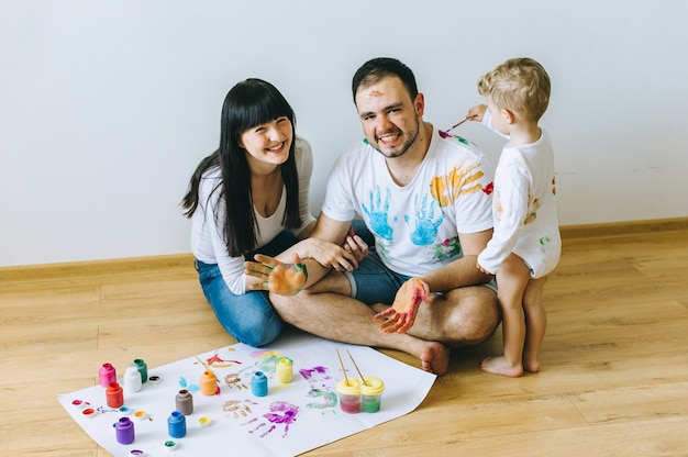 happy family son with parents and a cat painting a poster and one another with paints