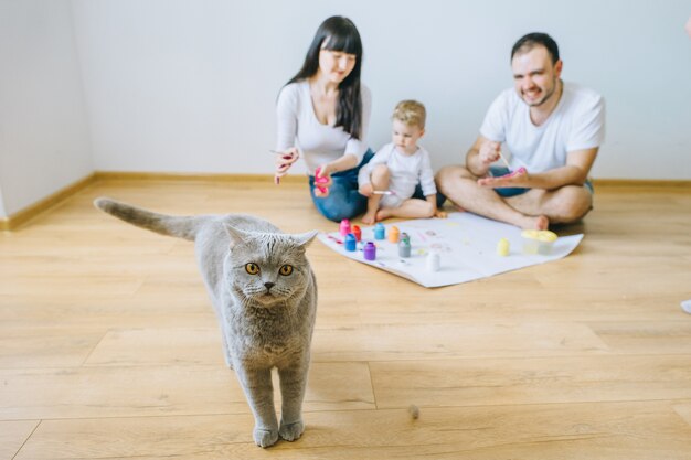 Figlio di famiglia felice con i genitori e un gatto che dipinge un poster