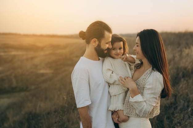 Happy family strolling in nature all together Joyful mother bearded father and little daughter walking on the field noise effect