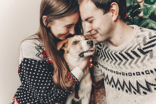 Happy family in stylish sweaters having fun with cute dog in festive room with christmas tree emotional moments merry christmas and happy new year concept happy holidays