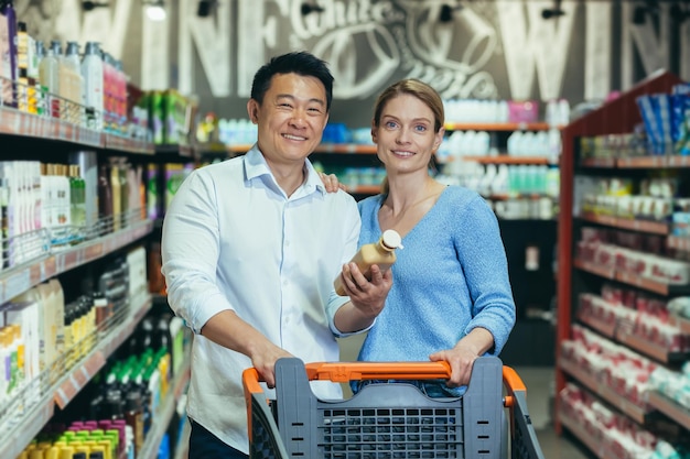Счастливая семья в супермаркете выбирает продукты, пара улыбается и смотрит в камеру