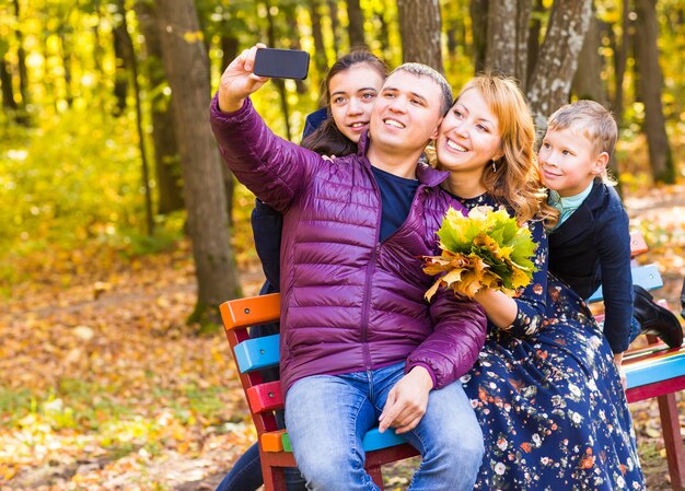 Photo happy family taking selfie by smartphone in autumnl park