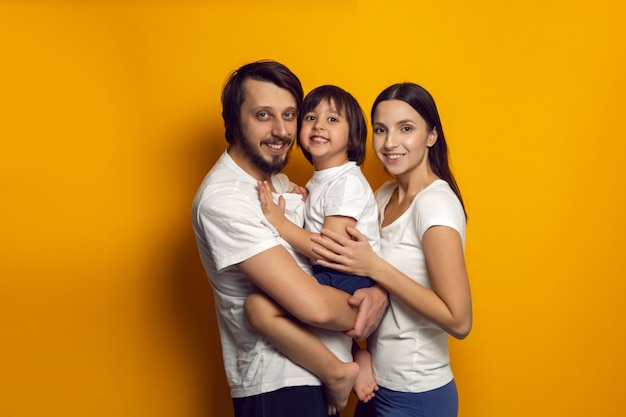 Happy family of three a boy and a child in white t shirts stand on a yellow wall