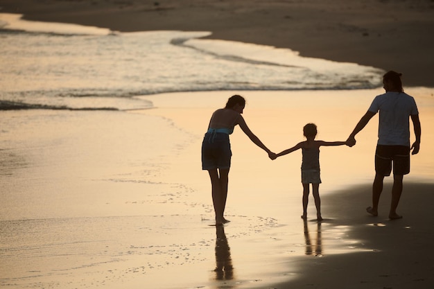 Happy family of three holding hands when walking on sandy beach at sunset