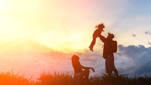 the happy family of three people, mother, father and child in front of a sunset sky.
