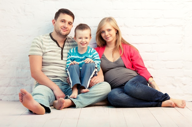 Felice famiglia di tre persone seduto sul pavimento vicino al muro