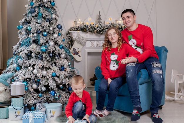 Счастливая семья из трех молодых мам, ожидающих рождения отца, и их маленького сына возле украшенной рождественской елки