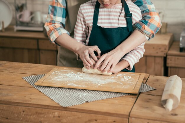 母の日にキッチンでケーキを焼く幸せな家族の時間の親子DIY。イースターのパンのために生地をこねる子娘を教える認識されていないアジアの女性のお母さん。女性と少女の手をクローズアップ