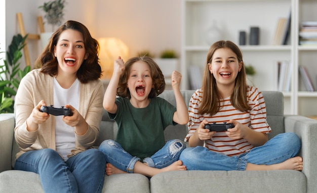 Happy family together Mother and her children girls playing video games People having fun at home