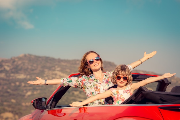 Happy family travel by car in the mountains people having fun\
in red cabriolet summer vacation concept