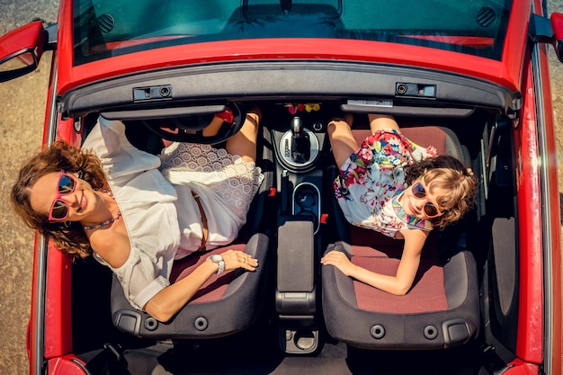 Happy family travel by car Woman and child having fun in red cabriolet Summer vacation and travel concept Top view