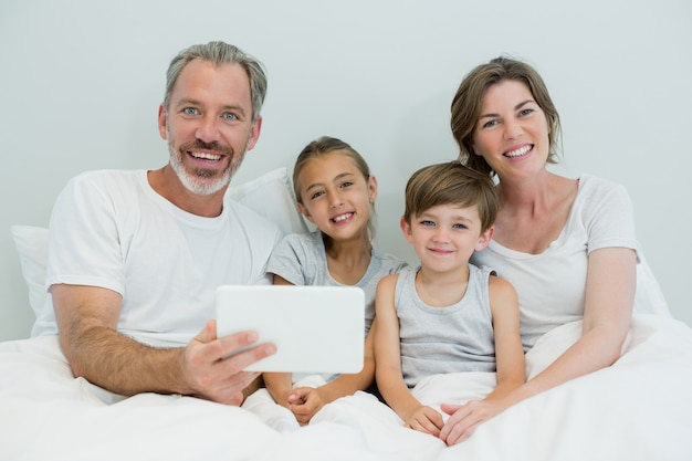 집에서 침실에 침대에 디지털 태블릿을 사용하는 행복한 가족
