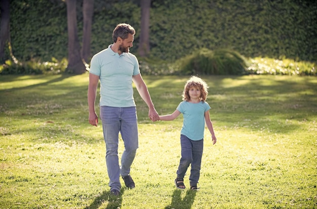 Happy family value childhood and parenthood parent leads little child boy on grass dad with kid boy on summer day parenting and fatherhood fathers day father and son walk in park